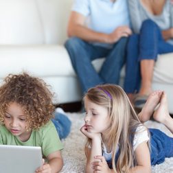Kids lying on the ground playing with a tablet.