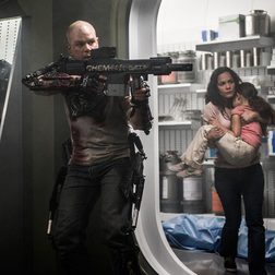 Matt Damon holds a gun next to a woman and child in Elysium.