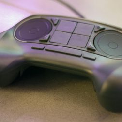 A Steam Controller from Valve on a surface. You can see two track pads on top with four buttons in the middle.