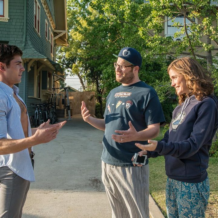 Zac Efron stands and talks to Seth Rogen and Rose Byrne in Neighbors.