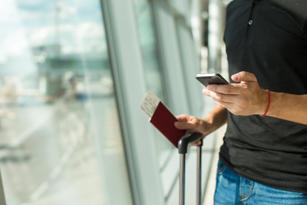 Man at airport with iPhone and airline ticket in hand.