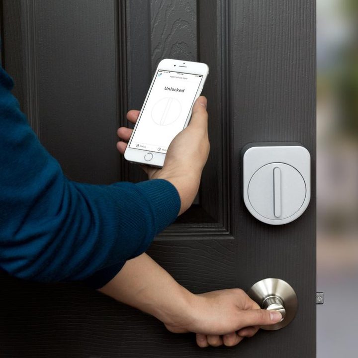 A person using their phone to unlock the Sesame Smart Lock on their door.