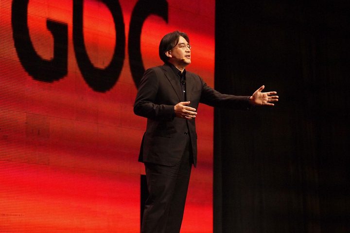 Satoru Iwata presenting at GDC in 2011 in front of a red GDC logo.