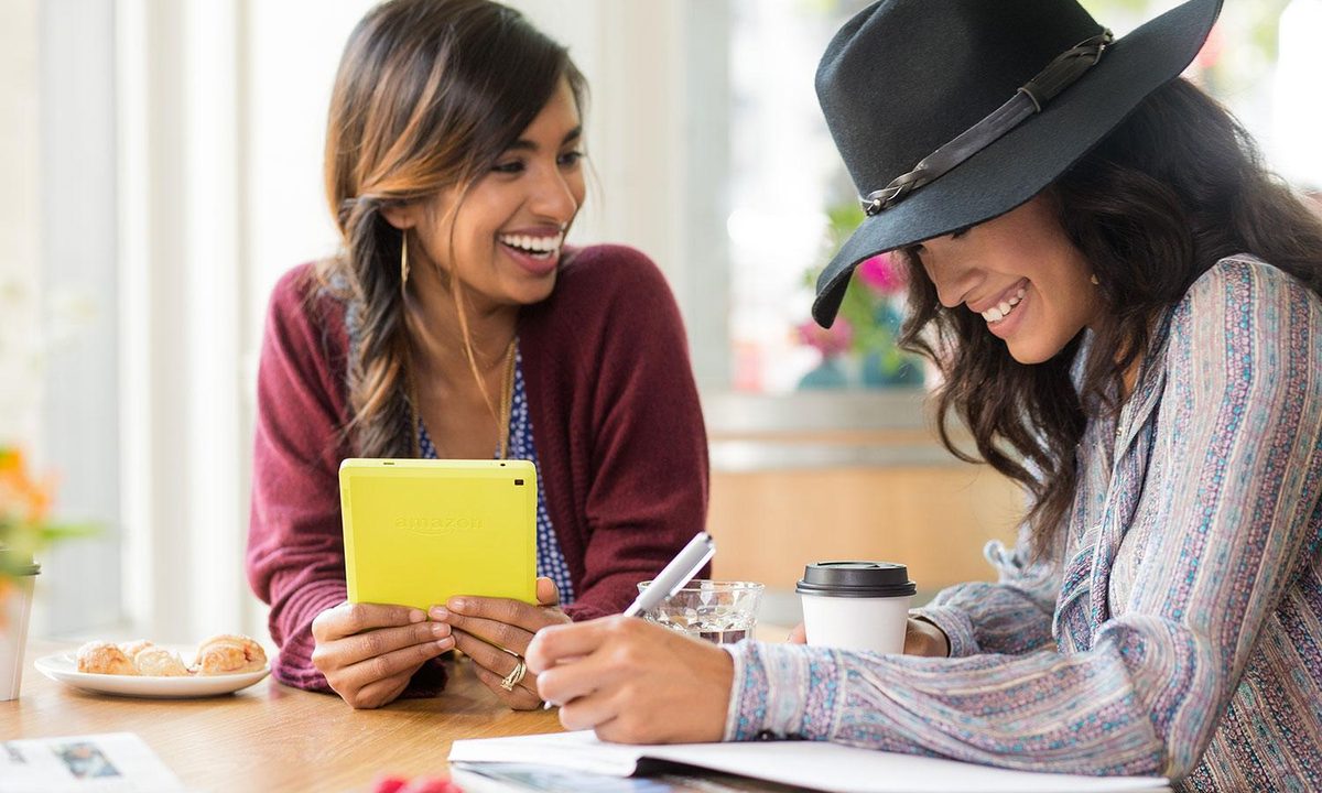 Two women working at a table with one holding an Amazon Kindle Fire.