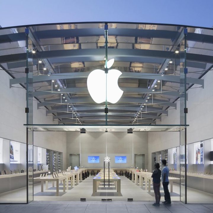 Two people look through the glass into an empty Apple store.