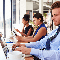 Three young professionals working on devices at a coffee shop bar.