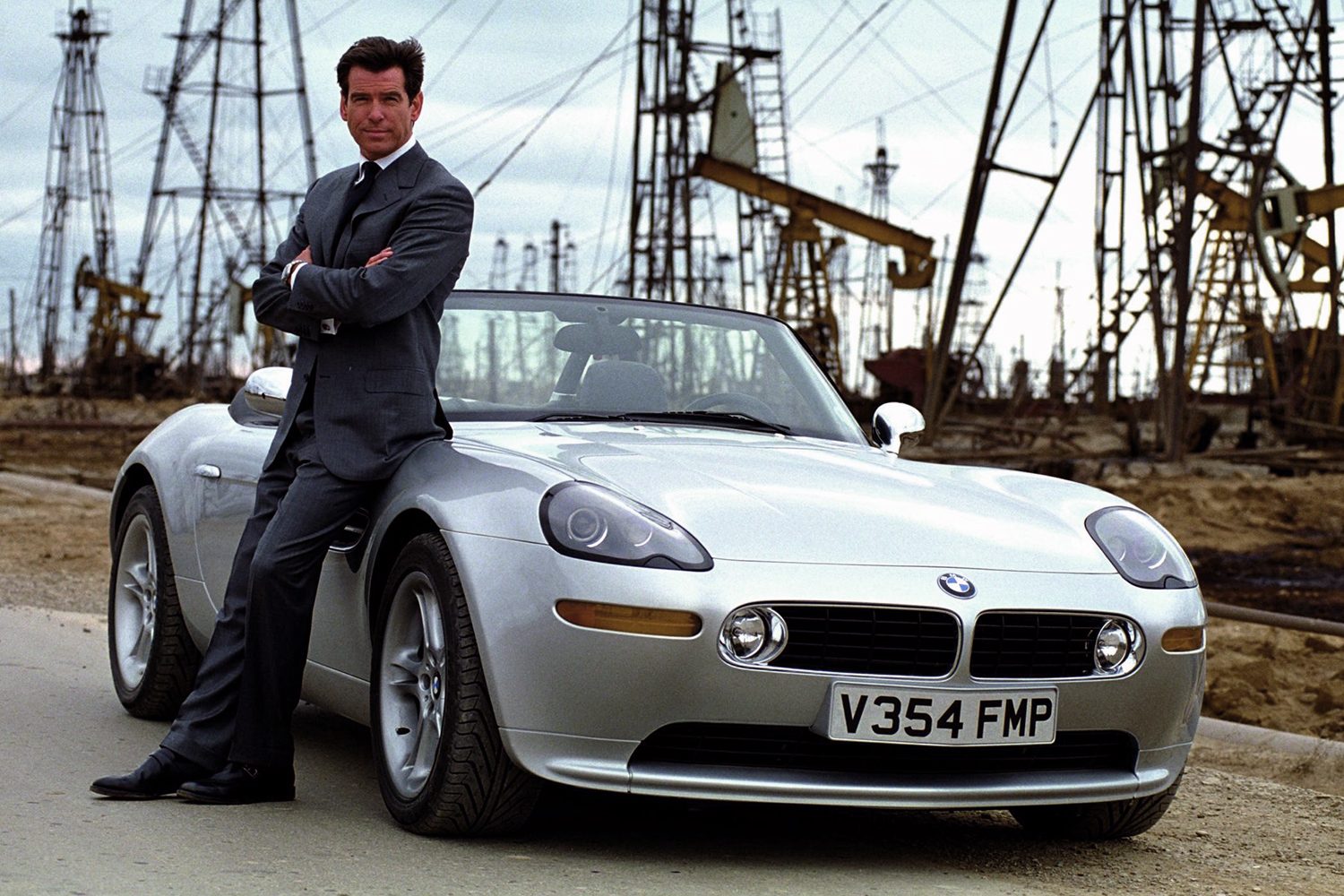 James Bond leans up against a car.