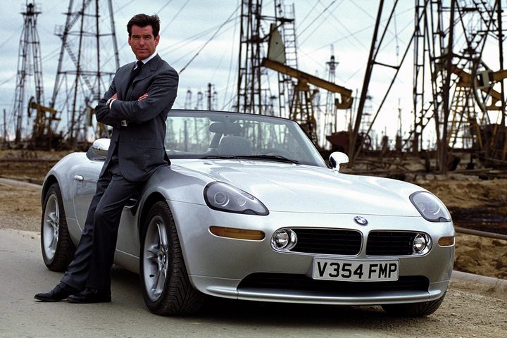 James Bond leans up against a car.