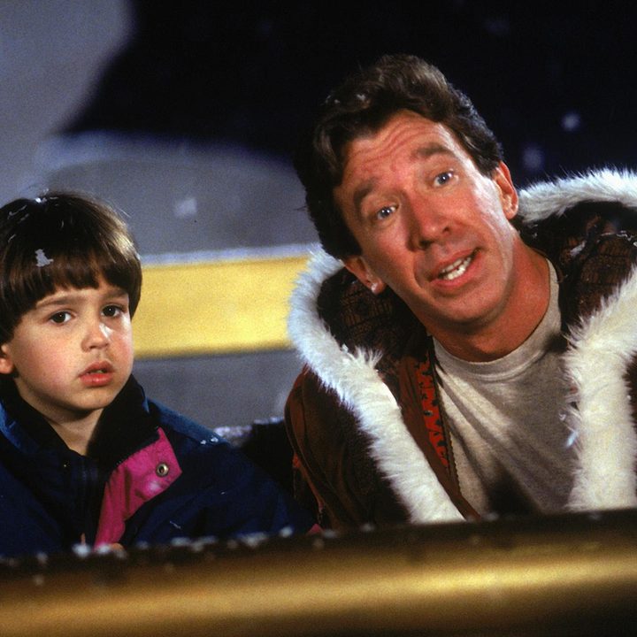 A man with Santa's coat sits in a sleigh with his son.