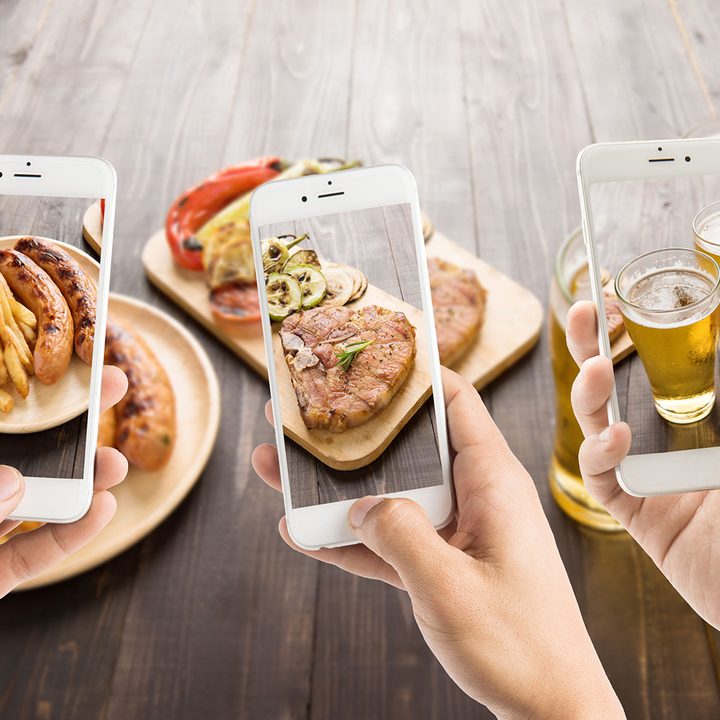 friends using smartphones to take photos of sausage and pork chop and beer.