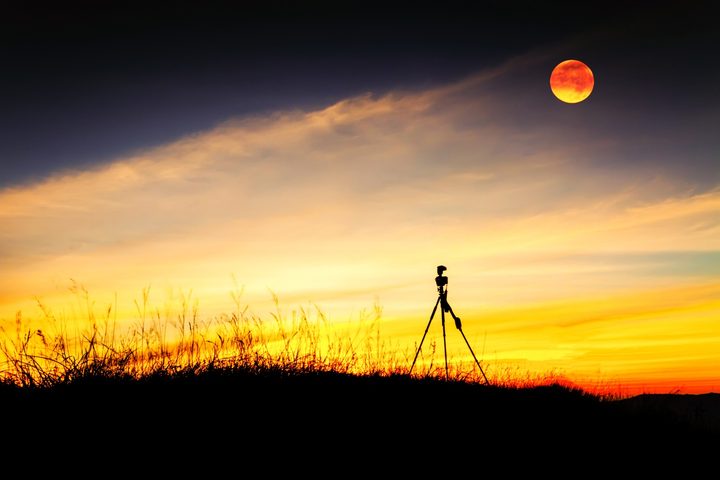 Tripod stand on mountain with moon at after sunset.