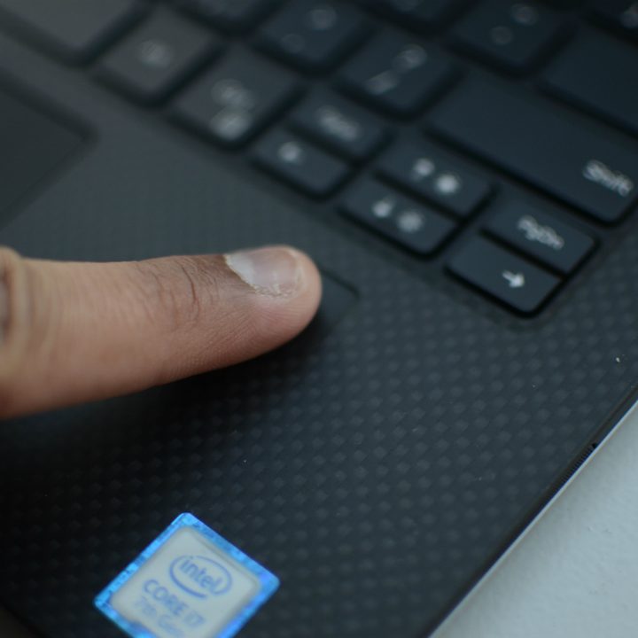 A finger pressing on a fingerprint reader on a laptop.