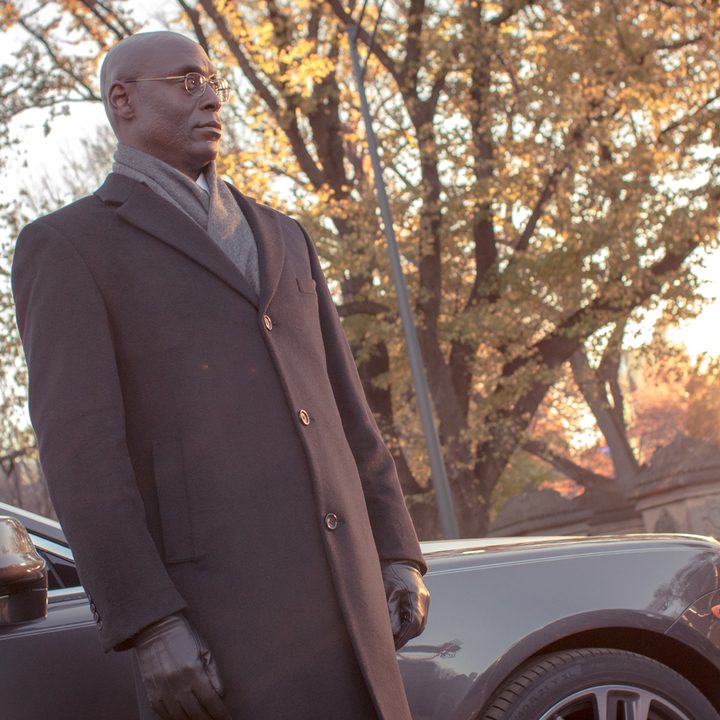 Lance Reddick stands in front of a car.