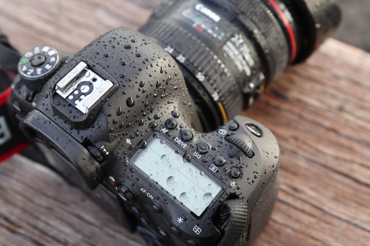Angled, top-side of Canon EOS 6D Mark II, covered in droplets, facing away diagonal right on wooden table