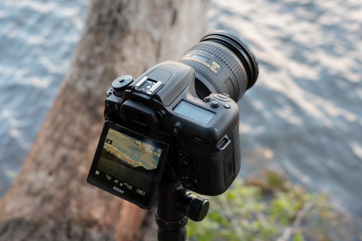 Back side of the D7500 angled to the right sitting on a tripod with the screen extended out