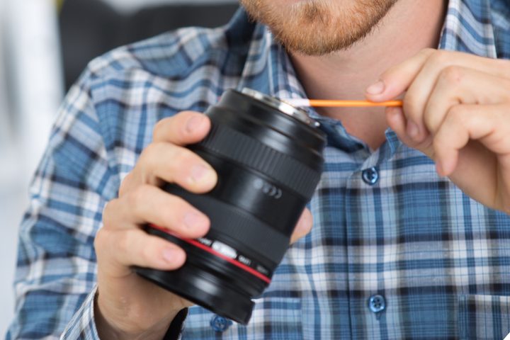 Camera technician cleans a DSLR camera lens.