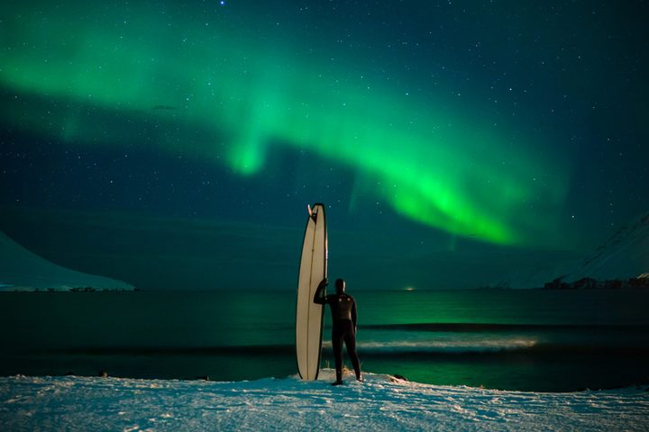 surfer standing under aurora borealis