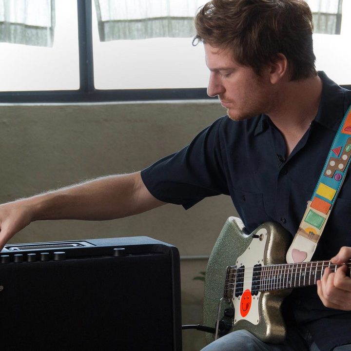 A man holding an electric guitar adjusts an amp.