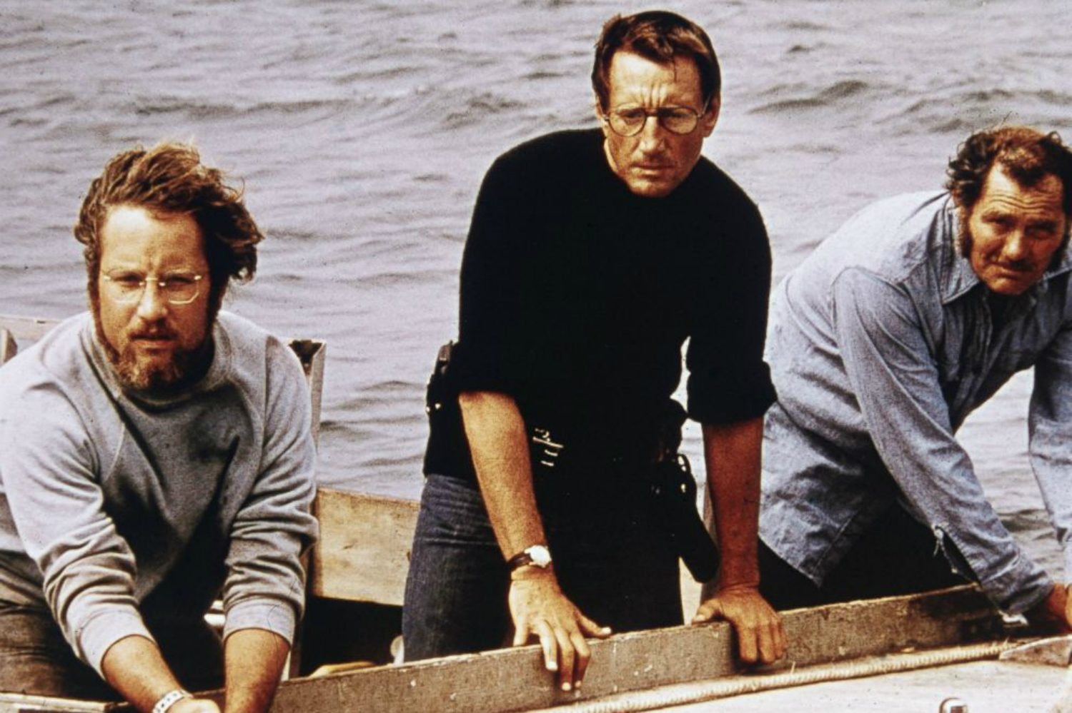 Three men stand in a boat and stare into the ocean in "Jaws."