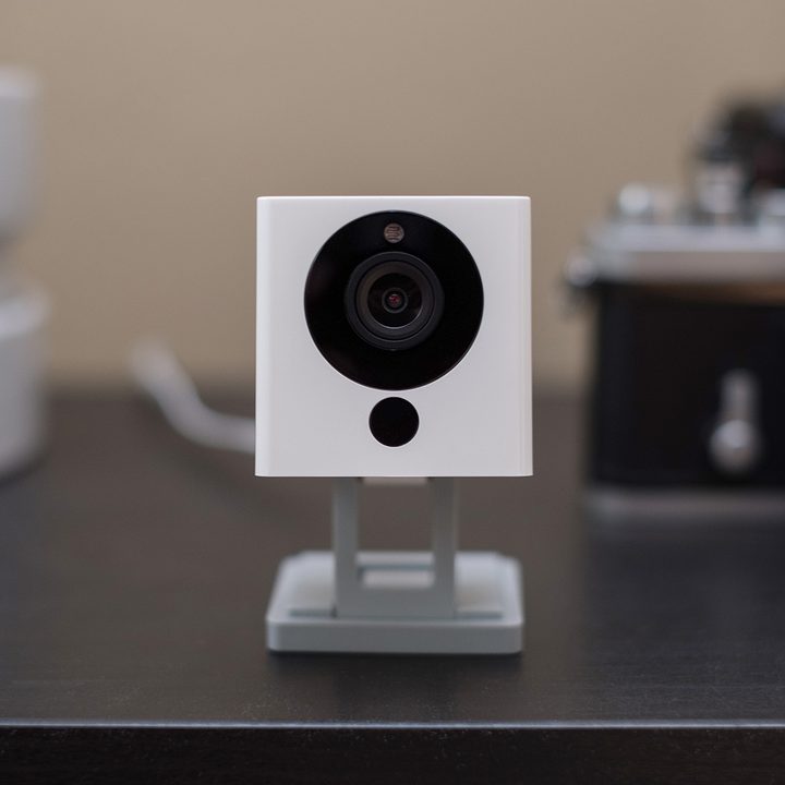 The WyzeCam sits on a desk with a camera in the background.