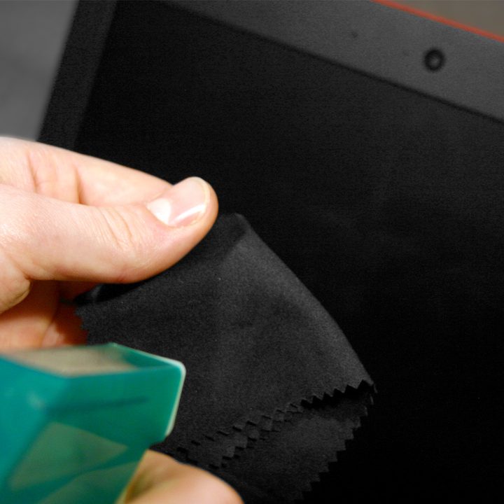 Person holding a microfiber cloth and spraying it with a cleaning solution.