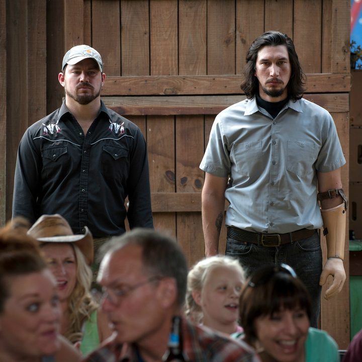 Channing Tatum and Adam Driver stand next to each other in the back of a room in "Logan Lucky."