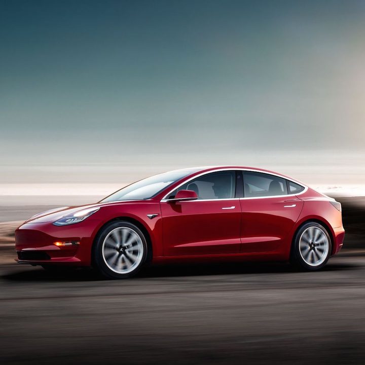 A red Tesla Model 3 at dusk.