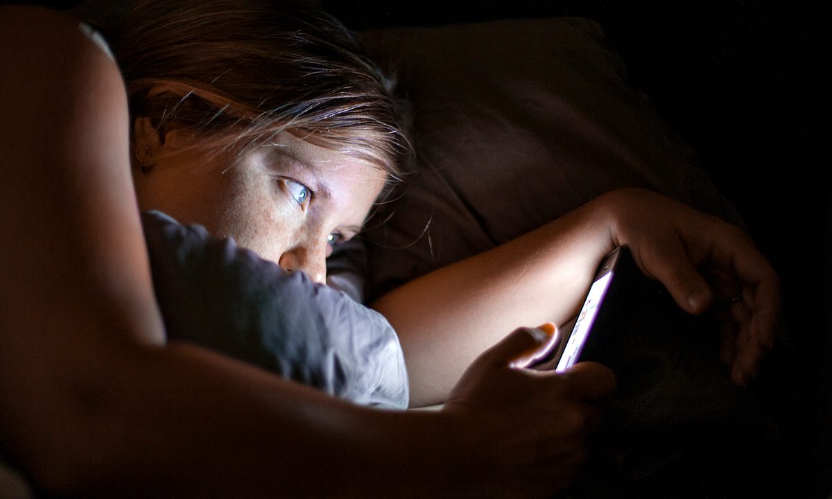 woman using cell phone in bed at night