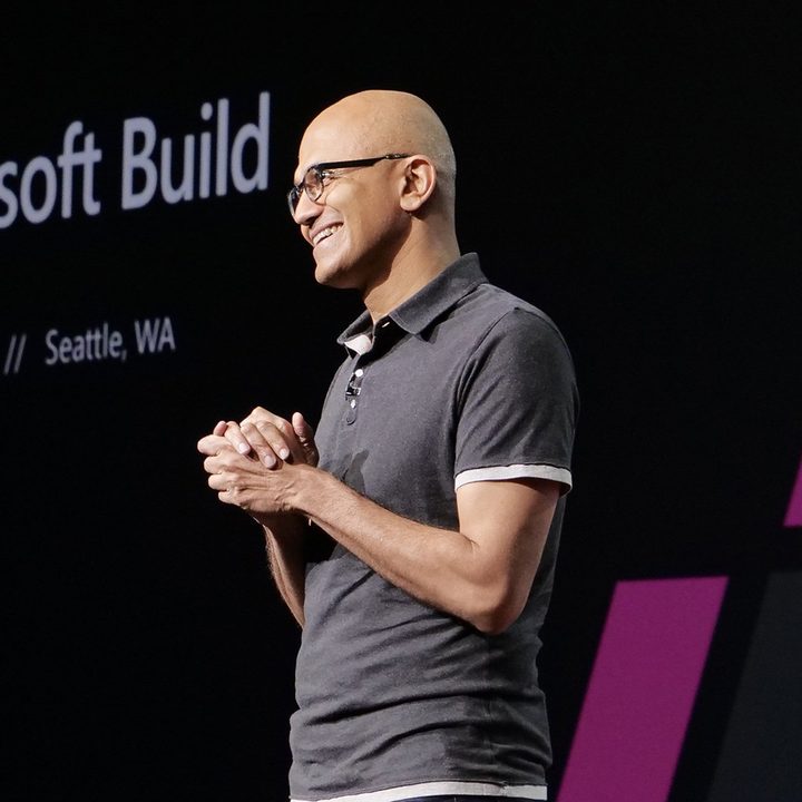 Microsoft CEO Satya Nadella standing onstage in a welcoming pose.