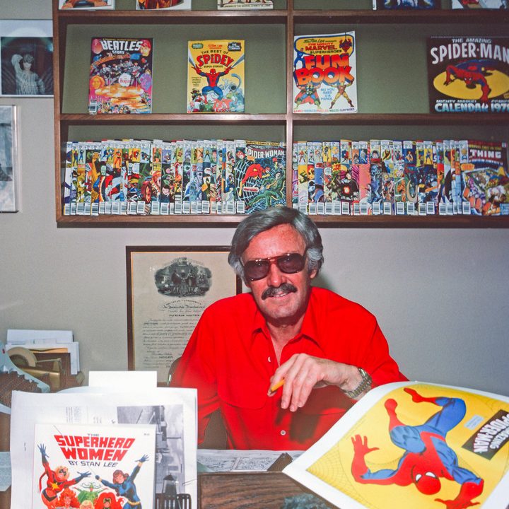 A younger Stan Lee, sitting in his office in front of comics