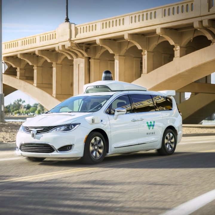 A Waymo One autonomous car drives under a bridge.