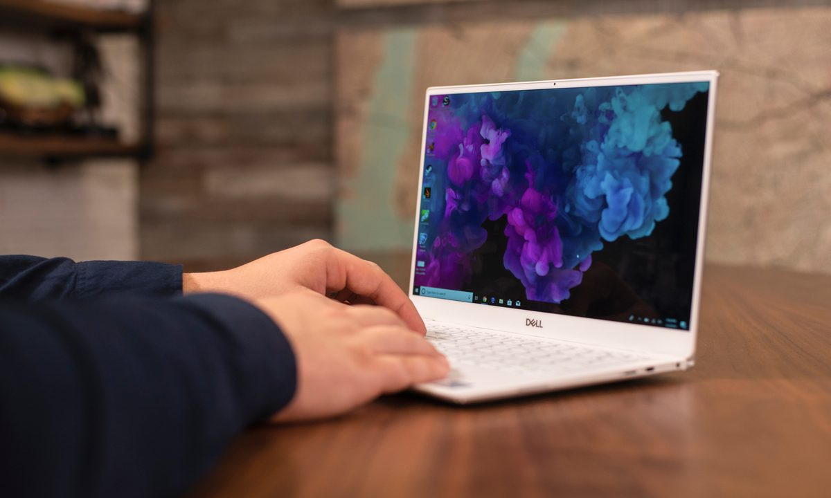 A person's hands resting on a 2019 Dell XPS 13 laptop as it sits on a table.