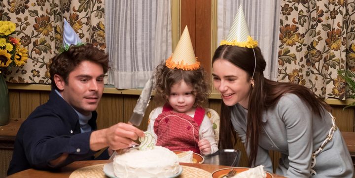 A man and woman sit around a young girl at a table with a birthday cake.