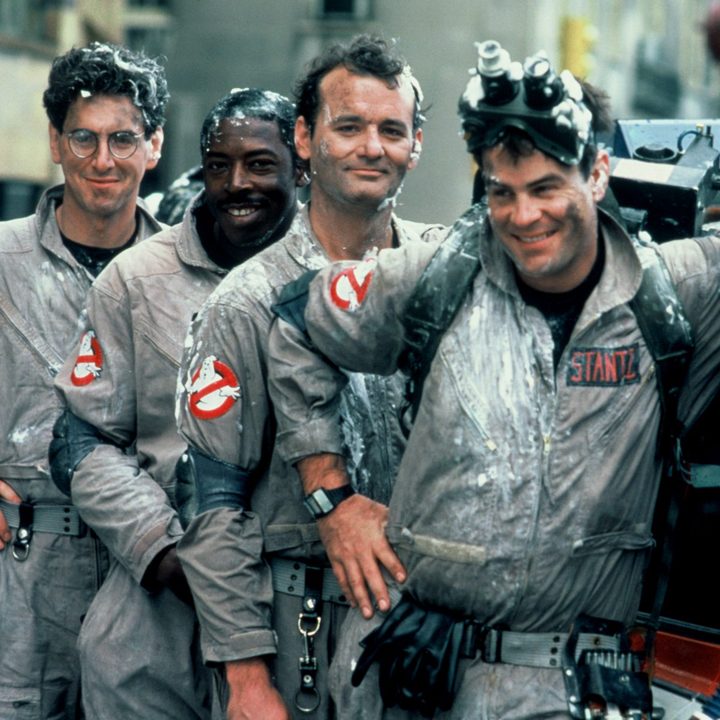 All four original Ghostbusters stand in a line covered in slime.