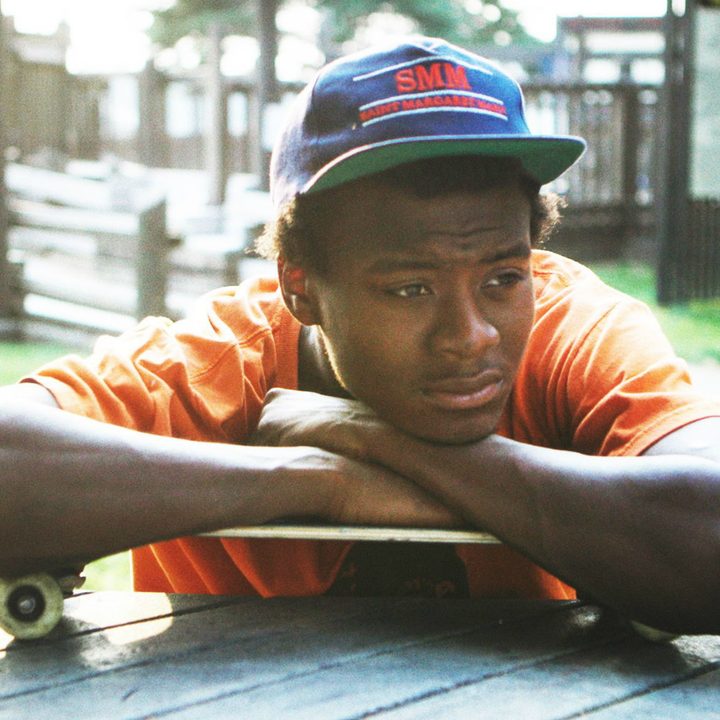 A male pus his hands on skateboard and leans on it.