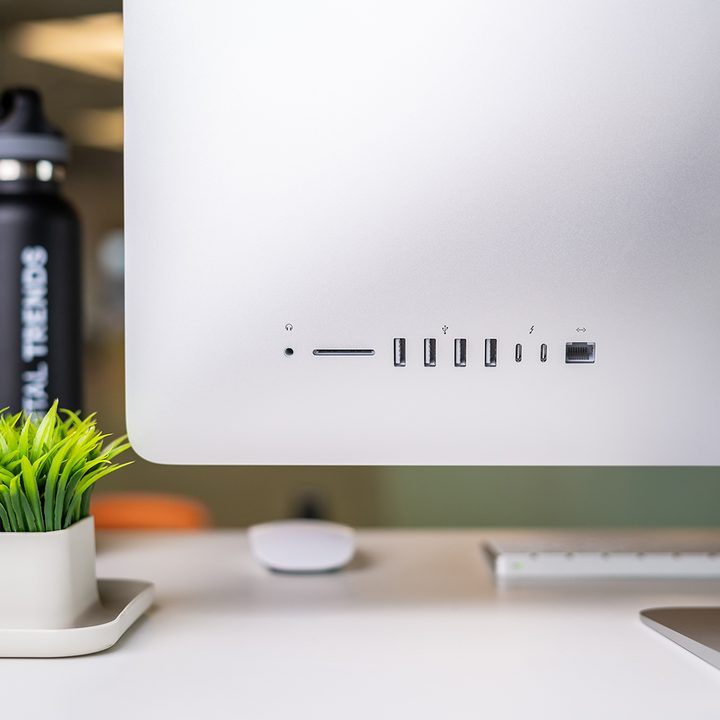Rear view of an iMac sitting on a white table next to a potted plant. A view in which you can see the iMac's selection of ports.