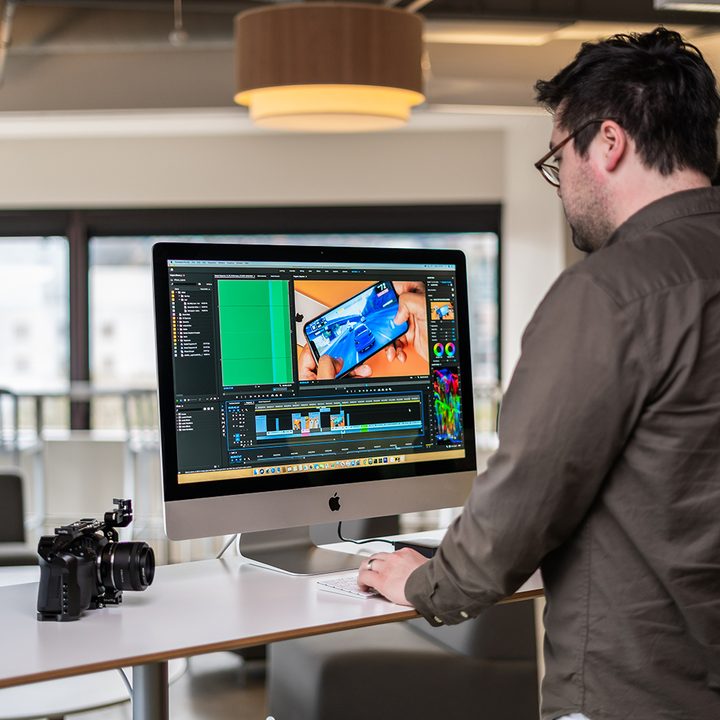 A man standing in front of an iMac with a camera on the desk.