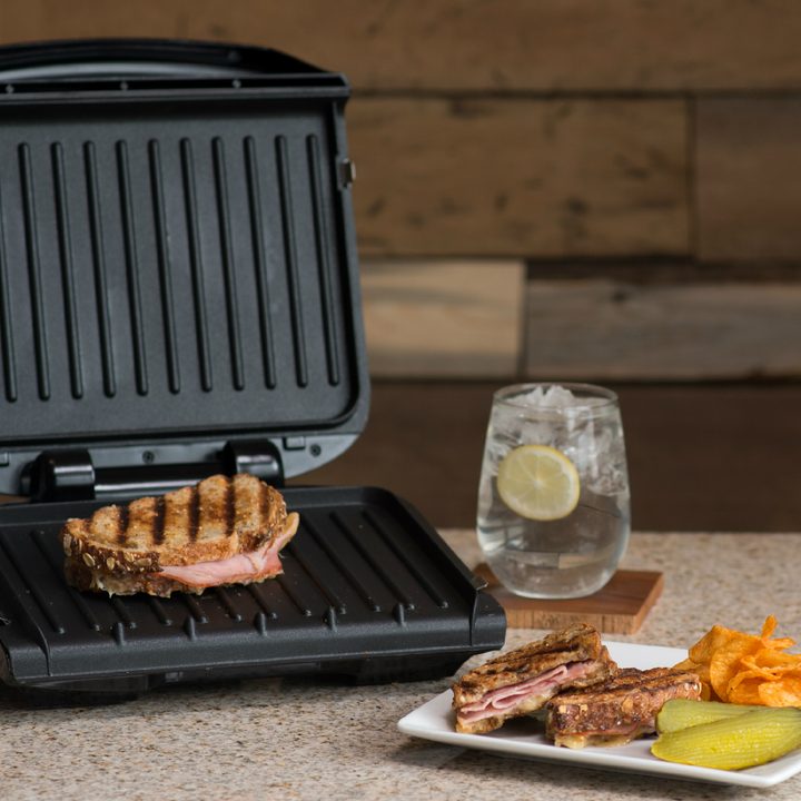 An indoor grill open with a panini on it next to a plate of food and a drink.