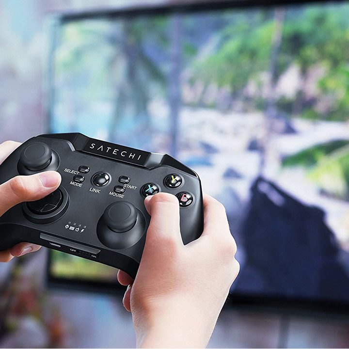 Hands hold a controller while playing a game on TV.