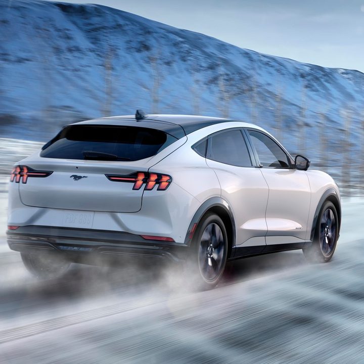 White Ford Mustang Mach-E driving in the snow.