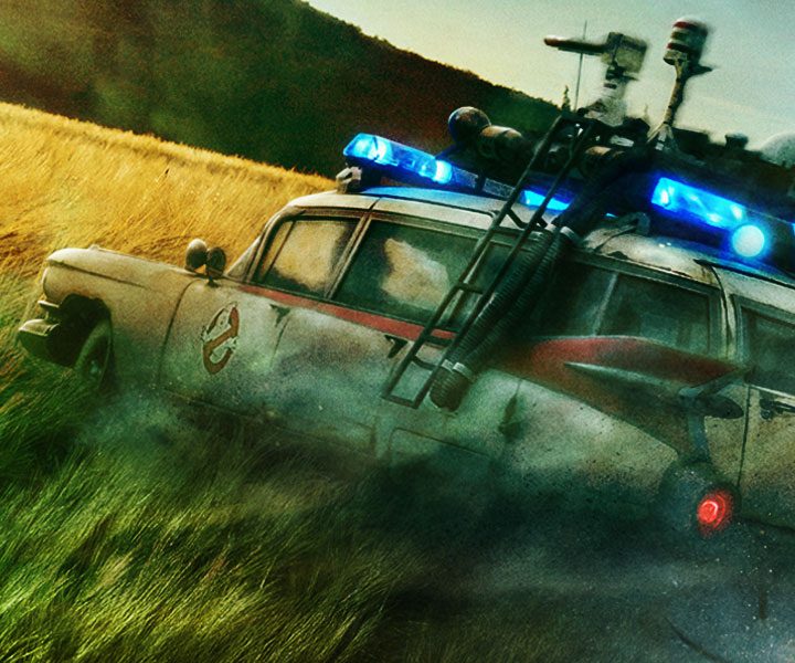 The famous Ecto-1 Ghostbusters car driving through a field.