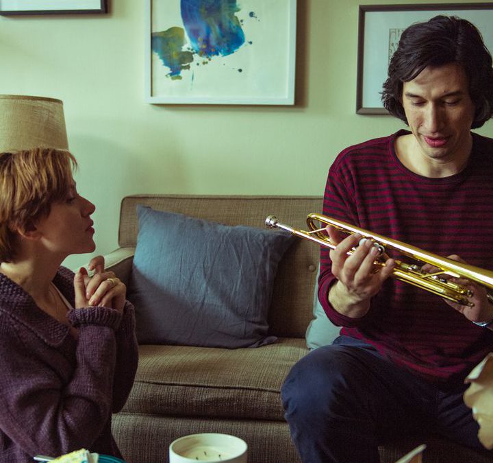 Adam Driver holds a trumpet next to Scarlett Johanson.