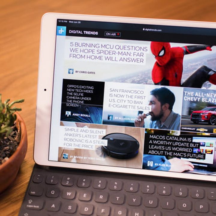 iPad sits on a keyboard on a table, with a potted plant next to it.