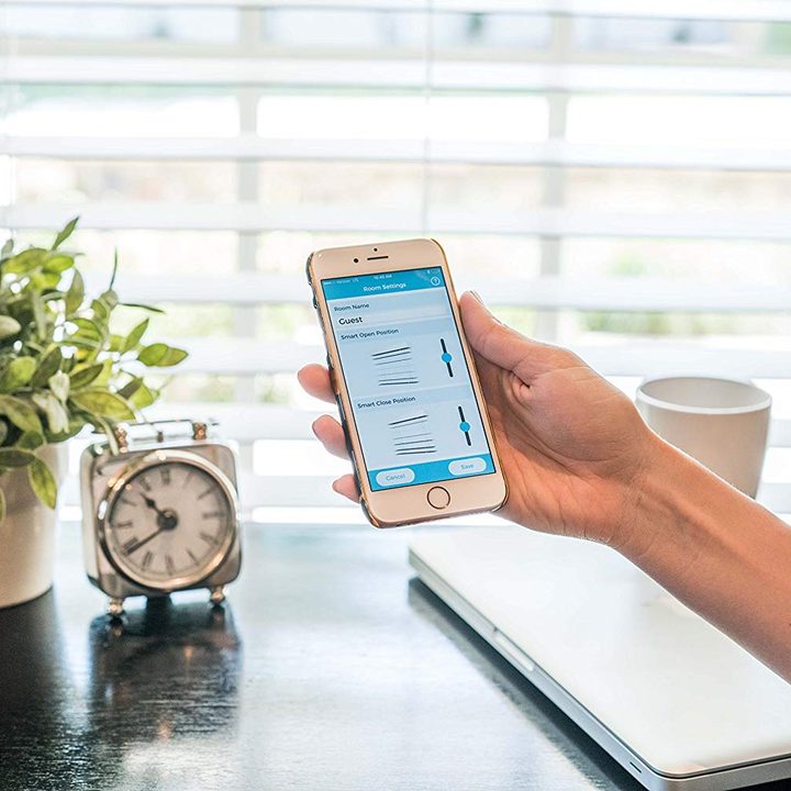 A smartphone with a blinds app in front of opened blinds.
