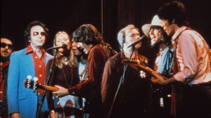 A group of singers stand around a mic.