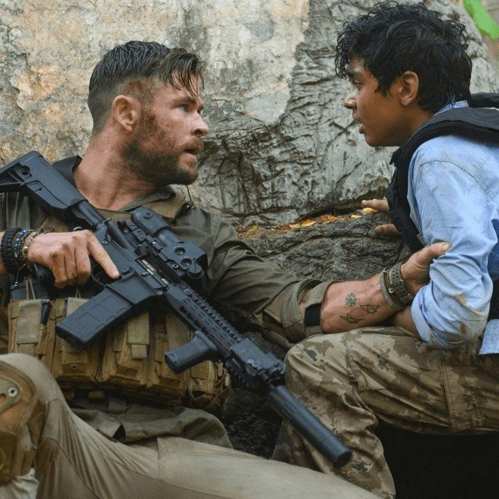 Chris Hemsworth holds a kid and a gun in Extraction.
