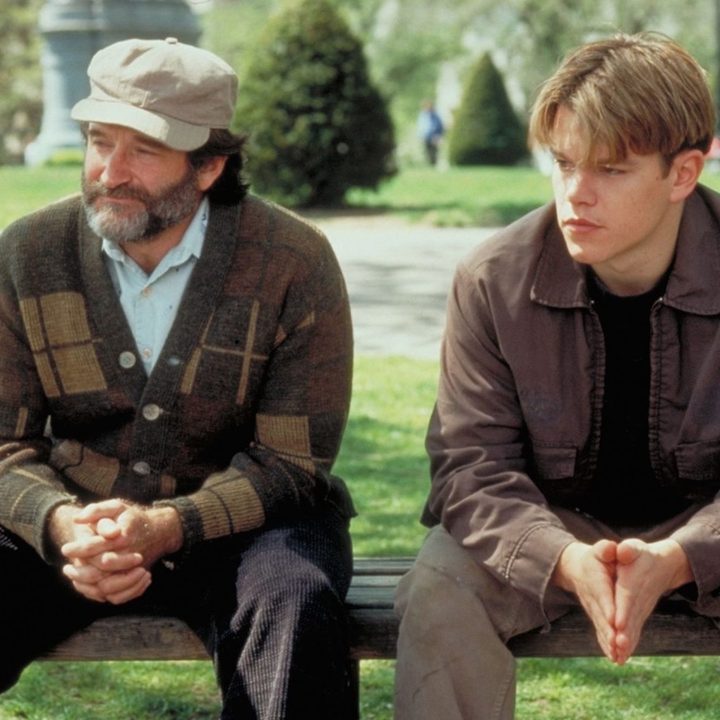 Robin Williams and Matt Damon sit next to each other on a bench.