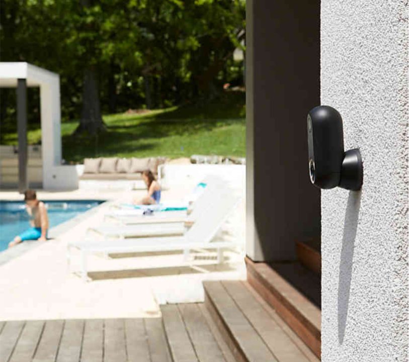 Canary home security camera on the side of a home in front of a pool.