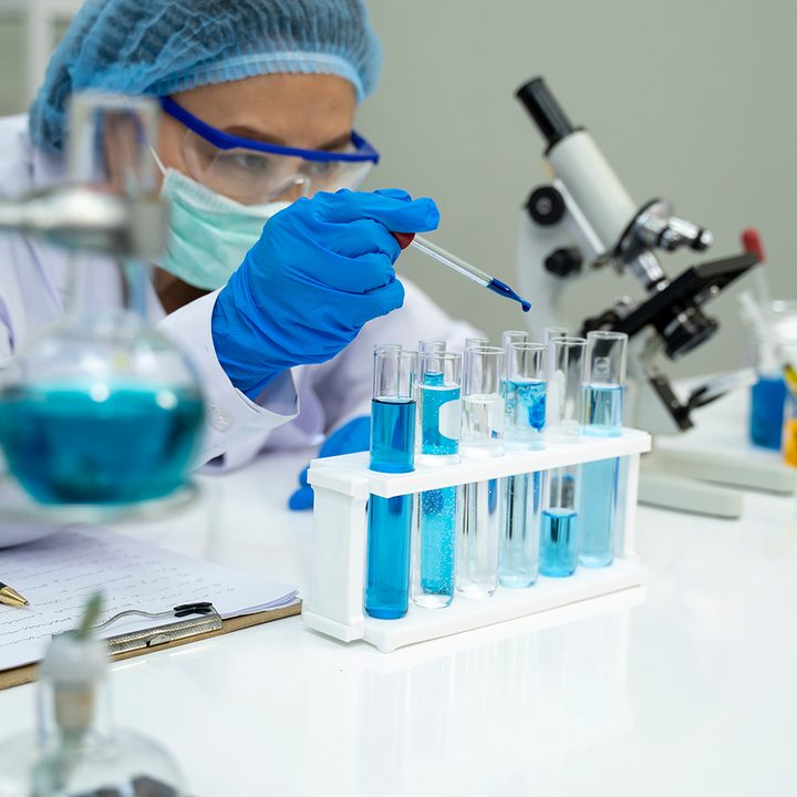 Scientist in laboratory working with an eyedropper, test tubes, and blue liquid and surrounded by various lab equipment.