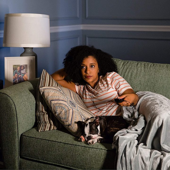 A woman lies on a couch holding a Roku remote watching TV.
